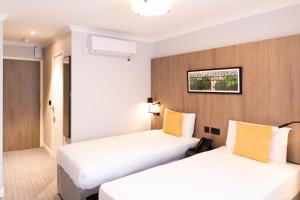 伦敦王子广场旅馆的配有白色和黄色枕头的酒店客房的两张床