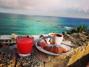 特罗佩阿Mediterranean Boutique Hotel的在岩石上一边享用咖啡和羊角面包一边欣赏海洋美景