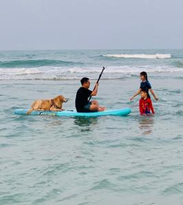 华欣Nichahome Luxury Villa的海面冲浪板上的男人和两个孩子以及狗