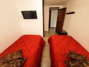 PácoraHotel Paucura的一间卧室配有两张带红色床单的床和电视。