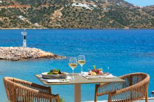 阿基欧斯尼古拉斯Wyndham Grand Crete Mirabello Bay的海滩上的一张桌子,上面放着两杯葡萄酒和食物