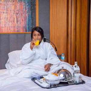 尼亚美Radisson Blu Hotel & Conference Center, Niamey的坐在床上喝一杯果汁的女人