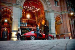 伦敦伦敦圣潘克拉斯万丽酒店的男人和女人在大楼前走过一辆红色汽车