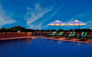 拉杰果德Fortune Park JPS Grand, Rajkot - Member ITC's Hotel Group的游泳池畔的两把椅子和遮阳伞