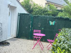 Croissy-BeaubourgMaison studio Le bois fleuri的两把粉红色的椅子和一张粉红色的桌子,一只蝴蝶在栅栏上