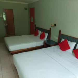 MukahHighway Inn的两张位于酒店客房的床铺,配有红色枕头