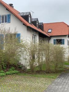 HuglfingFerienwohnung 2 in Huglfing im Herzen vom 5 Seen Land Oberbayern的白色的房子,有红色的屋顶和灌木丛