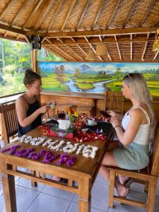 珀尼达岛Kubu Penida Villa的两个女人坐在木桌边,吃着食物