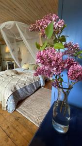 库雷萨雷Cosy guesthouse with sauna and outdoor kitchen的睡床旁边的桌子上装有紫色花的花瓶
