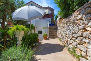 木洛希尼Apartments Valeria, Mali Lošinj的石墙旁的白色遮阳伞