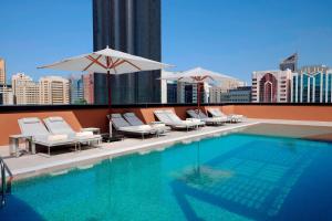 阿布扎比阿布扎比万豪国贸中心庭院酒店的一座大楼内的游泳池,配有椅子和遮阳伞