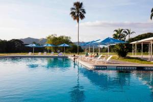 MaracayMarriott Maracay Golf Resort的一个带蓝色遮阳伞的大型游泳池,且有人坐在椅子上