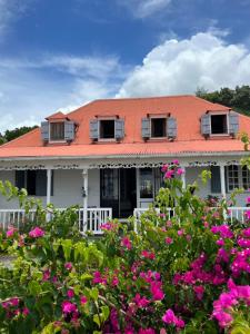 圣克洛德Habitation La Reine du Camp Chambres d'Hôtes的白色的房子,有橙色的屋顶和粉红色的鲜花