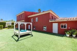 马拉加Ohana Luxury Villa with Heated Pool的红色房子前面的院子,有白色秋千