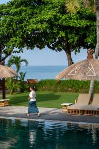 金巴兰Jimbaran Puri, A Belmond Hotel, Bali的一位在海边游泳池边散步的女人