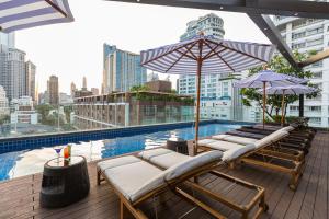 曼谷Hotel Icon Bangkok Sukhumvit 2的大楼内带躺椅和遮阳伞的屋顶游泳池