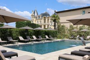 圣艾米隆格兰德巴拉伊城堡度假温泉酒店的大楼前的带椅子和遮阳伞的游泳池