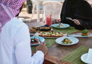 艾阿卡艾美阿尔阿卡海滩度假酒店的一群坐在餐桌上的人,拿着盘子的食物