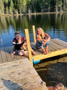 ColebrookLadd Pond Cabins and Campground, LLC的三个女孩坐在湖上的一个码头上