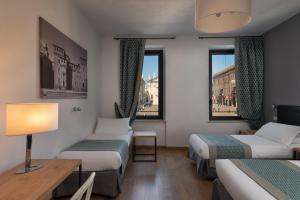 曼托瓦Hotel dei Gonzaga的客房设有两张床、一张桌子和两个窗户。