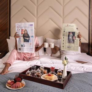 吉达Jeddah Marriott Hotel Madinah Road的躺在床上阅读报纸,带食物托盘的人