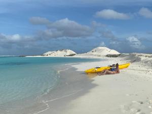 迪弗西Dhiffushi Island Villa的坐在海滩上的一个妇女,旁边是一艘黄色的皮艇