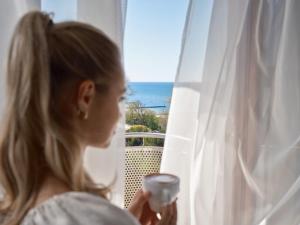 科沃布热格阿尔卡Spa酒店的一边拿着一杯葡萄酒一边看着窗外的女人