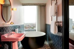 布鲁塞尔The Hoxton, Brussels的一间带粉色水槽和浴缸的浴室以及窗户。