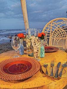 DibullaHotel Playa Paraiso的海滩上一张带盘子和酒杯的木桌
