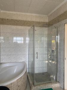 卢萨卡Samkab Legacy & comfort Ndeke (airport)的带浴缸和玻璃淋浴间的浴室。