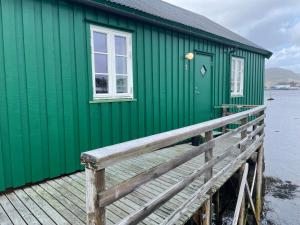 巴尔斯塔Kræmmervika Rorbuer - Rustic Cabins in Lofoten的绿色建筑,设有毗邻水面的木甲板