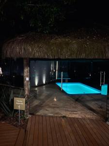 弗洛里亚诺波利斯Essência do Sol Pousada的茅草屋顶的夜间游泳池