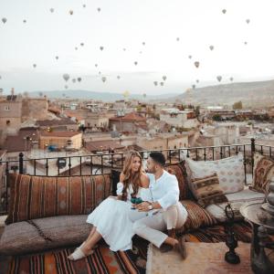 格雷梅Zara Cave Hotel的坐在阳台上的沙发上,坐上一对夫妇,带热气球