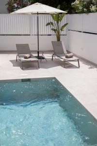 伊维萨镇Bossa Bay Suites with Private Pool - MC Apartments Ibiza的一个带两把椅子和遮阳伞的游泳池