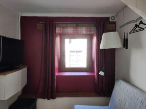 托尔明Casa di Volce - 1801 Stone House的一间卧室设有窗户、红色窗帘和电视
