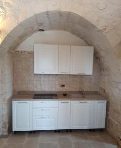 马丁纳弗兰卡Trullo Pentimelle的厨房配有白色橱柜和石墙