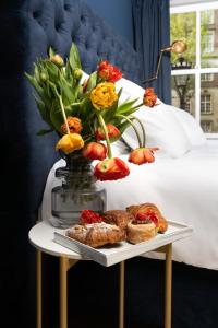 阿姆斯特丹Stanley Collection Hotel Hegra Amsterdam的一张桌子上摆着一盘糕点和鲜花,放在床边