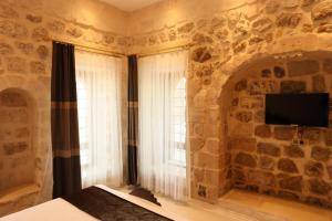 马尔丁Mardin Bey Konağı Hotel的一间卧室设有石墙、窗户和电视。
