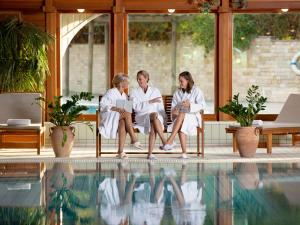 赫维兹Hotel Carbona Thermal Spa的三个身着白色长袍的女性坐在游泳池旁