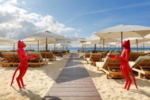 普拉亚登博萨Ushuaia Ibiza Beach Hotel - Adults Only-Entrance to Ushuaia Club included的海滩上的两座红色猫雕像,配有椅子和遮阳伞