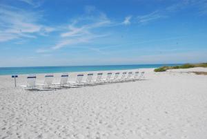 朗博特岛Gulf Tides of Longboat Key的坐在白色沙滩上的一排椅子