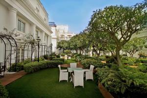 班加罗尔ITC Windsor, a Luxury Collection Hotel, Bengaluru的庭院配有白色的椅子和桌子,树木繁茂