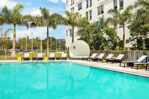 迈阿密雅乐轩迈阿密多拉酒店的一座带椅子和棕榈树的游泳池,位于一座建筑前