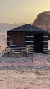 瓦迪拉姆Adam Bedouin camp的沙漠中一座黑白的建筑,配有椅子