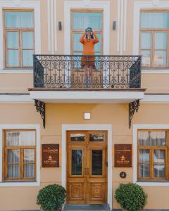 第比利斯The House Hotel Old Tbilisi的站在阳台上,画着一座建筑的画面的人