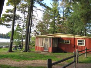 RhinelanderHoliday Acres Resort的湖边树林中的红色小屋