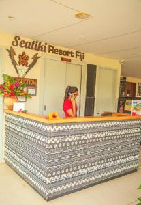 SigatokaSeatiki Resort Fiji On Coast的坐在柜台旁的一位女士在手机上讲话