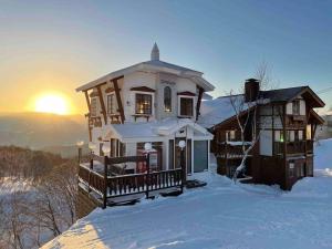 饭山市Blueberry Apartment的雪中的房子,背景是日落