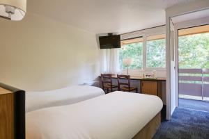 埃鲁维尔圣克莱Kyriad Caen Nord - Hérouville-Saint-Clair的酒店客房设有两张床、一张书桌和一个窗户。