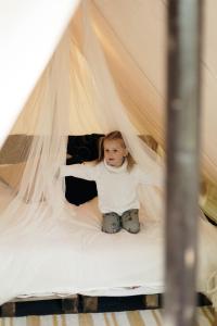 利加特内Glempings Jaunsaimnieki的坐在帐篷里的一个床上的小女孩